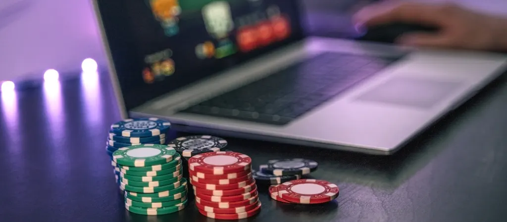 Szerencsej&aacute;t&eacute;k nyerem&eacute;ny ad&oacute;z&aacute;s online kaszin&oacute;ban, laptop mellett sz&iacute;nes p&oacute;kerzsetonokkal