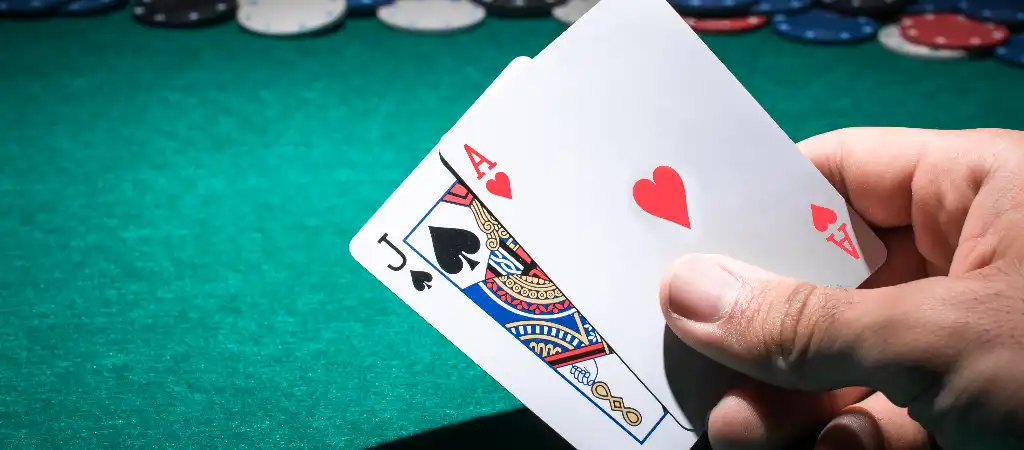 Blackjack szab&aacute;lyok &eacute;s j&aacute;t&eacute;kmenet, j&aacute;t&eacute;kos &aacute;sz &eacute;s bubi lapokat tart z&ouml;ld blackjack asztal felett