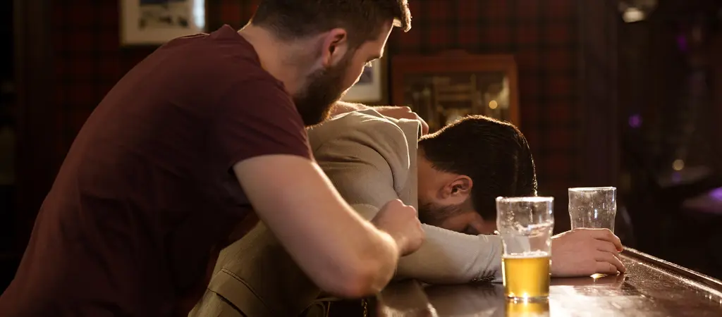 R&eacute;szeg f&eacute;rfi a pulton fekszik, mik&ouml;zben egy m&aacute;sik szem&eacute;ly t&aacute;mogatja, vizu&aacute;lisan bemutatva a szerencsej&aacute;t&eacute;k f&uuml;ggős&eacute;g kezel&eacute;se sor&aacute;n sz&uuml;ks&eacute;ges k&uuml;lső seg&iacute;ts&eacute;get